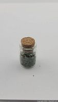 Closed glass jar filled with small emerald crystals, cork stopper sealed