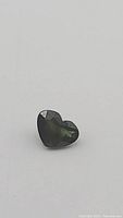 Close up of heart cut blue-green sapphire gemstone showing facets and color variations.