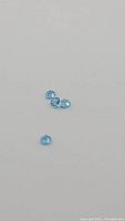 Four small trillion cut Swiss Blue Topaz gemstones on a flat surface, showing size and color.