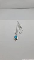 Full view of silver chain and turquoise pendant necklace laid flat on a white surface.