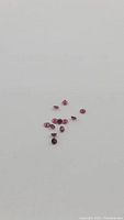Multiple small round-cut natural rubies arranged in a cluster on a white background, showing facet detail and color.