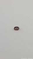 Oval cut deep raspberry pink purple tourmaline gemstone on white background, faceted surface visible.
