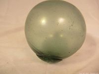 Top-down view of the spherical glass float showing its translucent green color and surface wear.