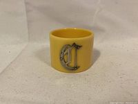 Full napkin holder showing the yellow color and the silver letter C on the front.
