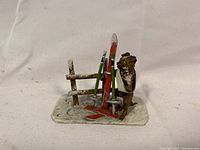 Cold painted bronze metal skiing dog figurine showing dog, skis, poles, and fence detail on snow-like base.