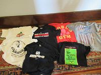 Seven T-shirts laid out showing logos and graphics including Chevrolet, gym logo, How The Grinch Stole Christmas, and more.
