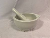 Side view of the ceramic mortar with pestle resting inside, showing the pouring spout and base shape.