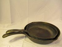 Two stacked black cast iron frying pans with long handles, showing general wear from use.