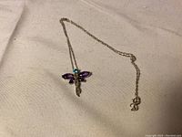 Photo shows the dragonfly pendant on the silver chain laid flat on a fabric surface.
