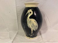 Full front view of a Tanglewood Pottery ceramic vase showing an oval form with dark blue background and cream-colored heron bird design.