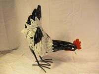 Side view of vintage metal rooster showing body painted in black and white with detailed leaf patterns.