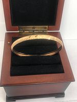 10K gold bangle displayed in open wooden box with black velvet interior