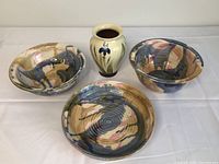 Full lot of four pottery pieces including two bowls, one high edge plate and one vase on white background.