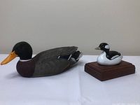 Two carved duck decoys side by side: larger male duck with detailed feather painting and smaller mounted duck on a wooden base.