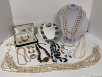 Full view of all costume jewelry pieces showing necklaces, pins, earrings, including several pearl strands and assorted bead necklaces.