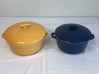 Yellow and blue Dutch ovens side by side on white cloth surface