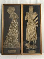 Front view of two gold brass framed rubbings side by side showing detailed medieval figures of a knight and a lady.