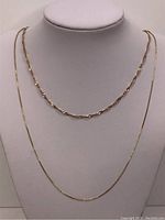 Two gold chains displayed on bust: twisted serpentine chain at top, box link chain below