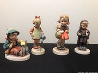 Group view of four Hummel figurines on black surface against white background