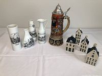 Photo of entire lot showing 4 Delft blue and white liquor house bottles, Swiss musical stein, German vases, Austrian pitcher and vase