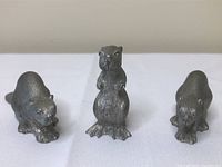 Three pewter beaver figurines positioned on plain surface showcasing standing and crouching poses.