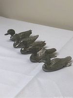Front angled side view of the five pewter duck figurines lined up with foot extended and showing detailed feathers.