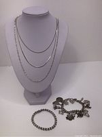 Overview of three chain necklaces displayed on bust with curb bracelet and charm bracelet on table.