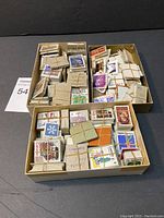 Three open cardboard boxes filled with numerous small bundles of vintage Canadian stamps secured with elastic bands or wire, arranged on a black surface.
