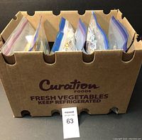 Six large ziplock bags containing thousands of postage stamps on paper inside a cardboard box.