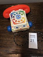 Top view of vintage Fisher Price Chatter Telephone toy showing white rotary dial with colorful numbers, red plastic receiver and black/white braided cord.