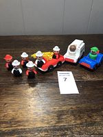 Overall group of Fisher Price emergency play figures and vehicles on wooden surface, showing all included items.