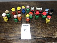 Group photo showing 18 Fisher Price original wooden Little People characters arranged on a wooden surface.