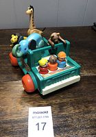 Vintage Fisher Price style safari set including plastic adventure vehicle with three little people peg figures and four animal toy figures (lion, elephant, giraffe, bear) arranged on table.