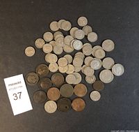 35+ old British coins laid out on a black surface, with varying sizes and metals including many silver-colored and copper or bronze-colored coins.