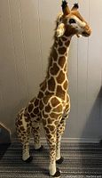 Full body view of the large stuffed giraffe showing detailed giraffe pattern and standing posture against a wall.