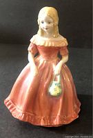 Front view of Miss Margaret figurine showing detailed facial features, coral dress, and green floral purse.