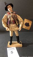 Front view of the Romanian doll highlighting the embroidered vest, cream folk costume, plastic face, and attached tag.