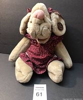 Front view of plush dog hand puppet sitting wearing burgundy floral dress, showing soft plush wrinkles and tag on ear.