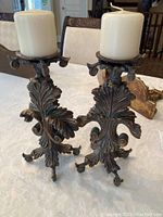 Front view of the two metal candle holders with white pillar candles on a table, showing their detailed design and size