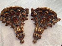 Pair of wall sconces shown from the top and a frontal side angle revealing the ornate leaf and scroll motifs with reddish-brown and gold finish.