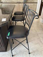 Three black metal bar stools lined up at kitchen counter showing design and condition