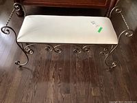 Top front angle of wrought iron bench with white cotton seat, showing ornate curled iron legs and upholstery condition.