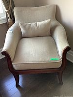 Front angled view showing upholstered armchair with wooden mahogany finish frame and beige seat cushion with matching lumbar pillow.