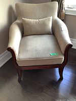 Front view of a Bombay Company upholstered armchair with cream/beige fabric and mahogany wood frame. Shows seat cushion, backrest, and lumbar pillow.