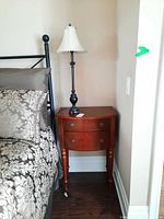 Night table positioned beside bed with decorative bedding, showing entire table and lamp on top.