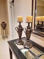 Pair of antique style metal candle holders on glass table with cream pillar candles on top.