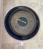 Full photo of the round wall clock showing the clock face with Roman numerals and decorative frame.