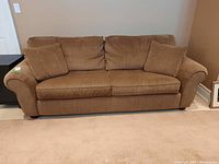 Front view of a brown 3-seater couch with two side cushions on beige carpet.