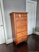 Front view of tall wooden dresser showing all six drawers with metallic handles, light wood finish.