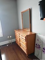 Dresser with 6 drawers and matching framed mirror standing against a wall with wood flooring.
